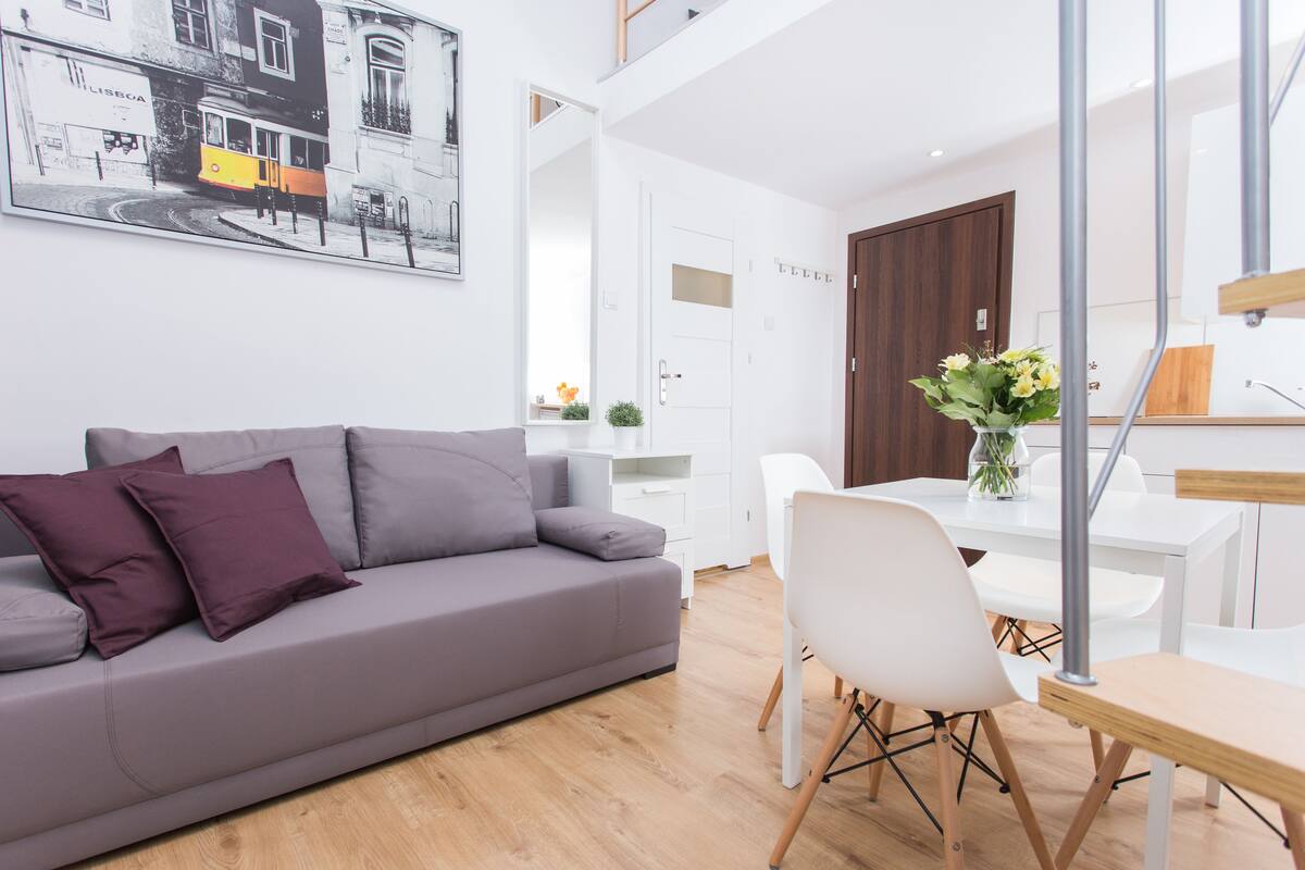Uma sala de estar moderna com um sofá cinzento, cadeiras brancas e uma mesa de jantar.