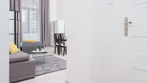 A modern living room with a grey sofa, a small coffee table, and a dining area with a white cabinet and chairs.