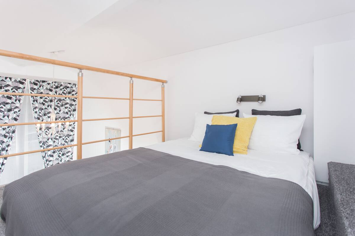 Um quarto moderno com uma cama, uma cabeceira de madeira e uma janela com cortinas estampadas.