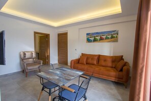 A living room with a brown leather sofa, a dining table with chairs, and a painting on the wall. - Pegasus Hotel & Villa (Fethiye)