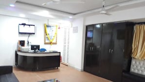 A reception area with a desk, chairs, a television, and a large wardrobe. - Swagatham Lodging (Navi Mumbai)
