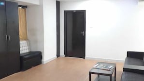 A spacious living area with a large sofa, a coffee table, and a black cabinet. - Swagatham Lodging (Navi Mumbai)