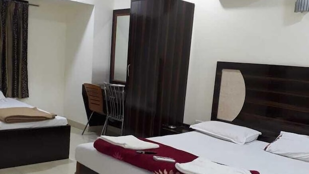A hotel room with a large bed, a desk, a chair, a wardrobe, and an air conditioning unit. - Swagatham Lodging (Navi Mumbai)