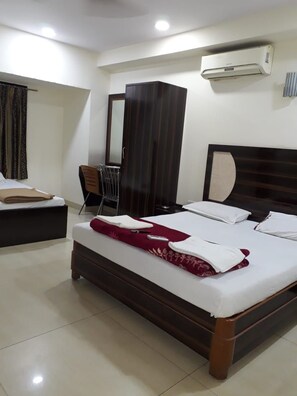 A hotel room with a bed, a desk, a chair, an air conditioning unit, and a wardrobe. - Swagatham Lodging (Navi Mumbai)