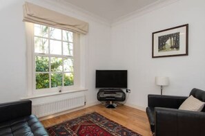 Ein Wohnzimmer mit großem Fenster, einem Flachbildfernseher, einer schwarzen Ledersofa und einem gemusterten Teppich.