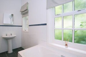 Une salle de bain avec un lavabo blanc, une baignoire et une fenêtre donnant sur un paysage verdoyant.