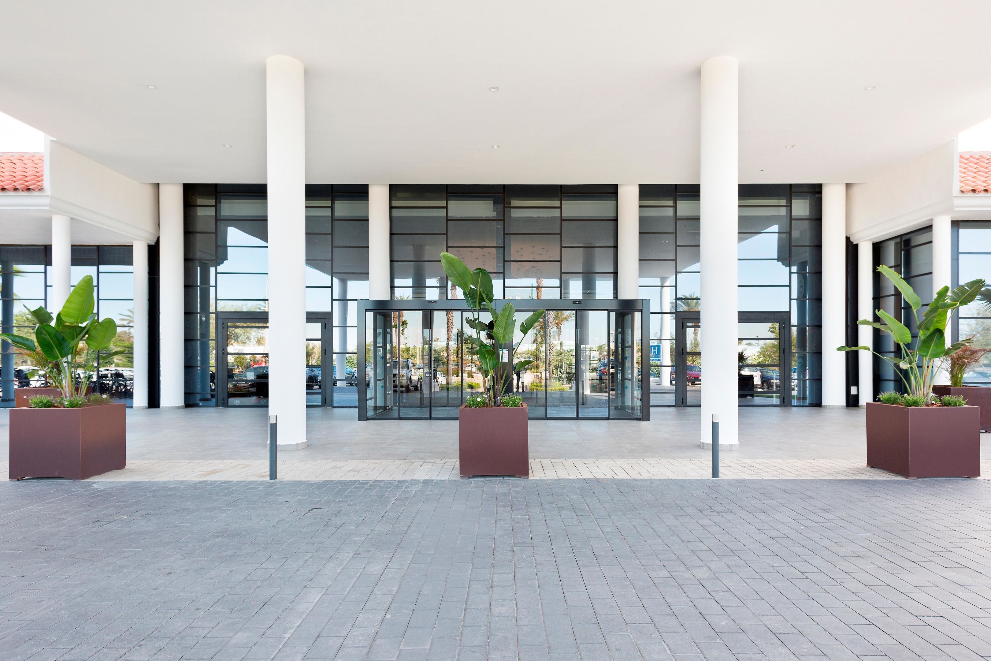Une entrée moderne, avec de grandes portes vitrées, des piliers blancs et des plantes en pot.
