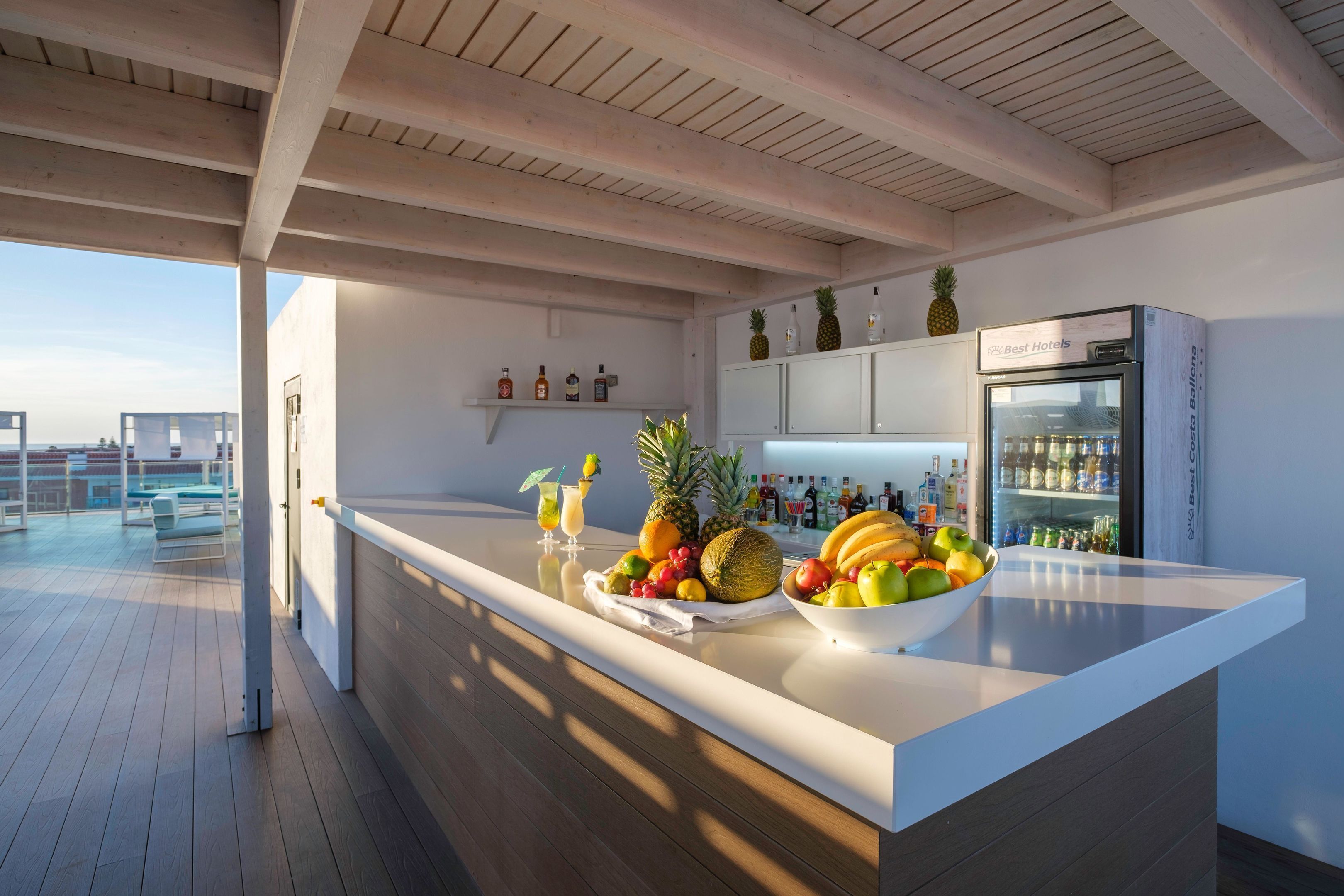Una cocina moderna con una isla grande, un refrigerador y una zona de bar con botellas y frutas.