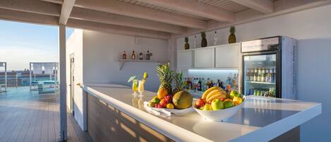 A modern kitchen with a large island, a refrigerator, and a bar area with bottles and fruits.