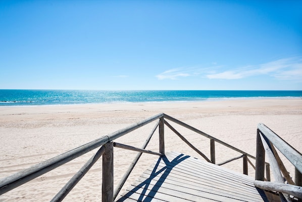 A wooden beach boardwalk leading to a sandy beach with a clear blue sky.