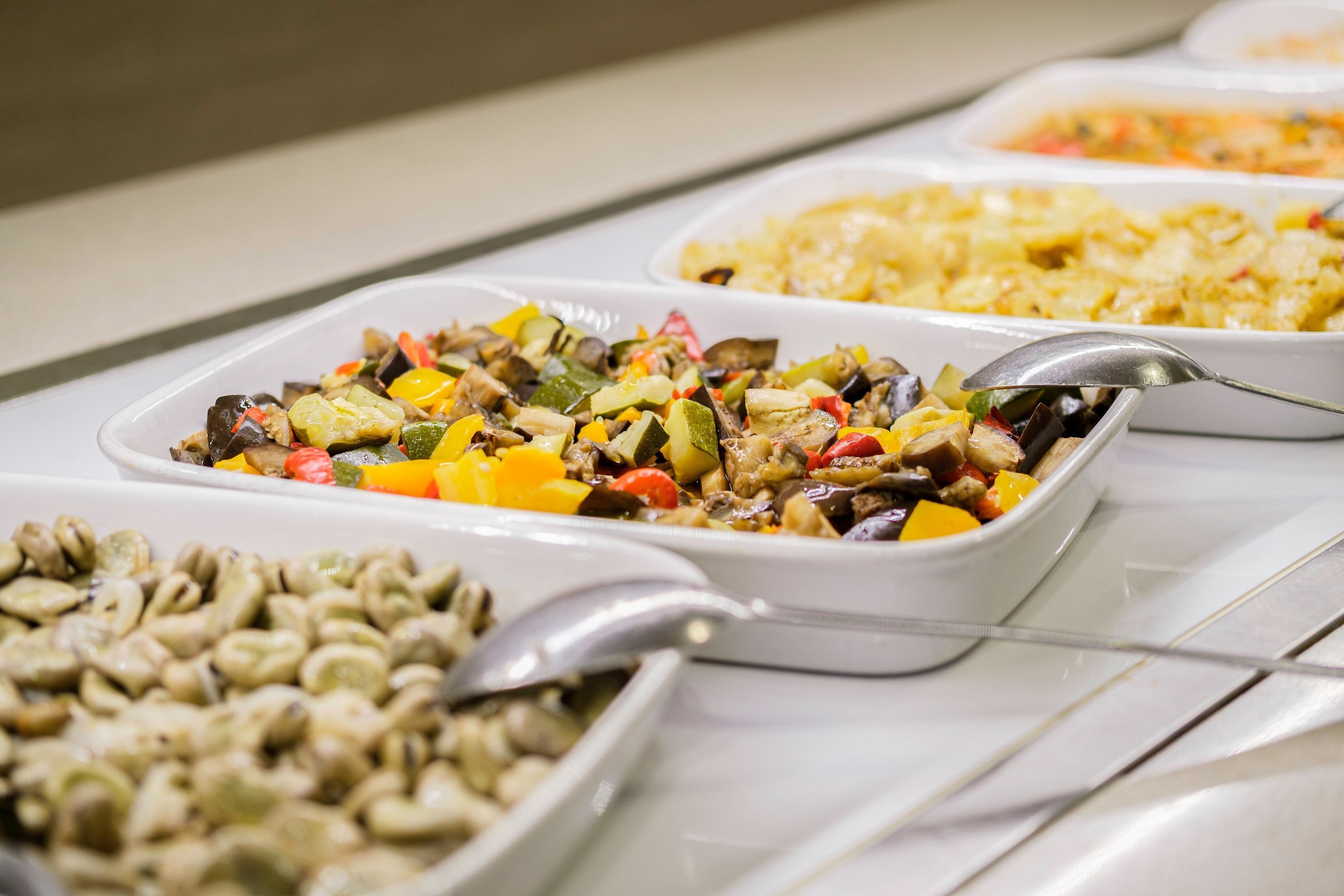 Un buffet con diversi piatti, tra cui un soffritto di verdure, pasta e un'insalata di fagioli.