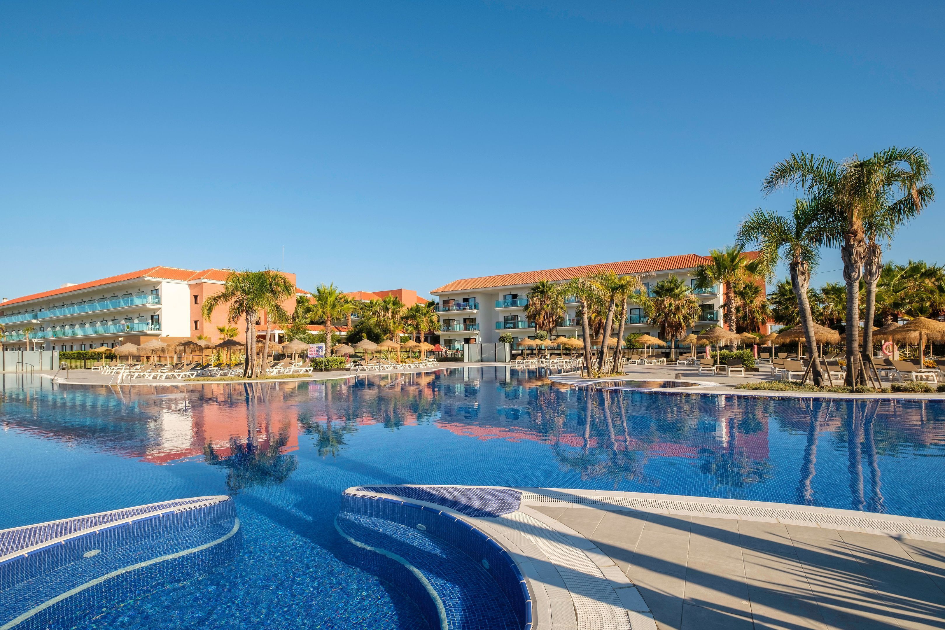 Una piscina resort con acqua cristallina, palme e alberghi sullo sfondo.