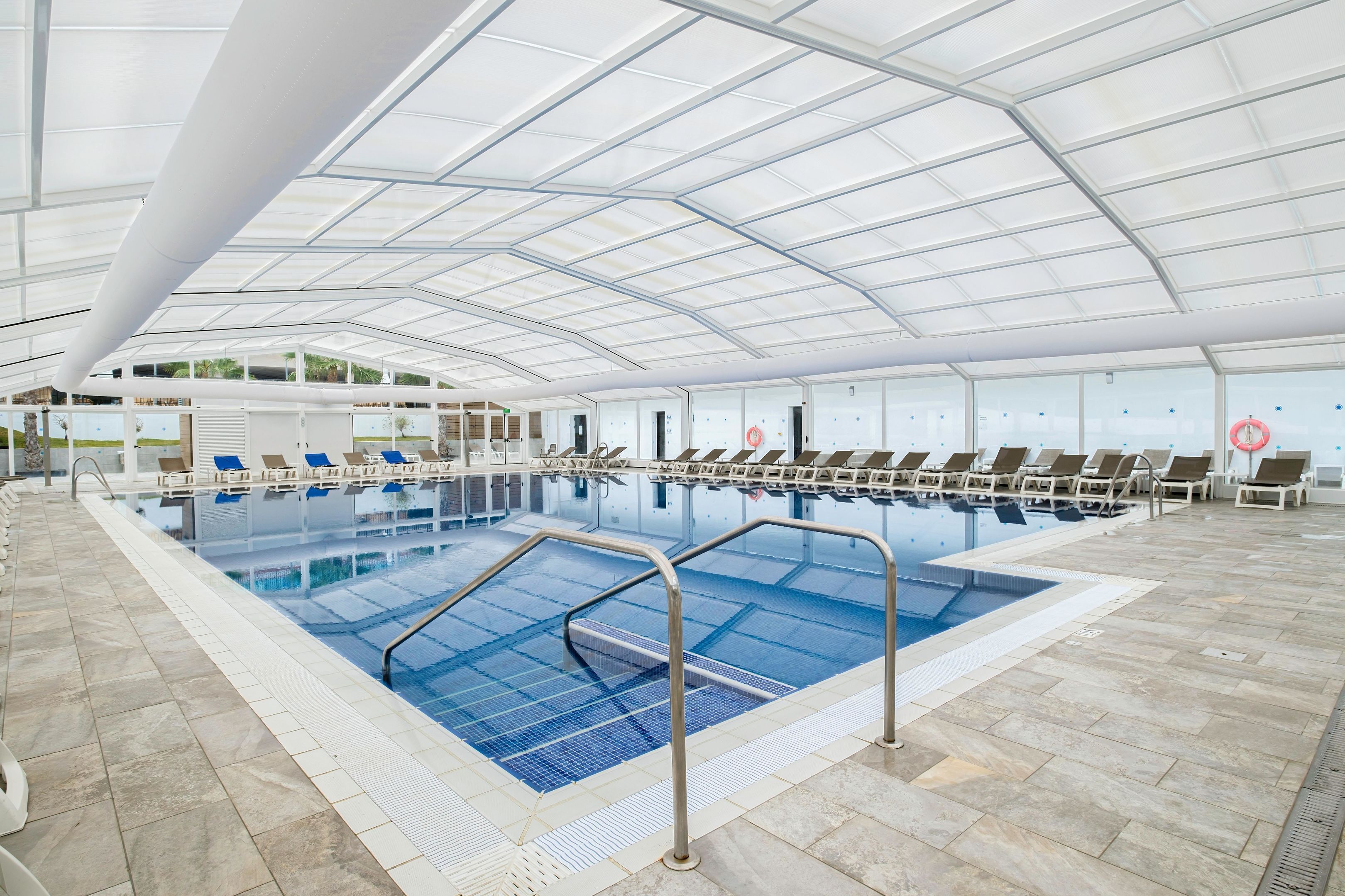 A large indoor swimming pool with multiple lanes, lounge chairs, and a covered roof structure.