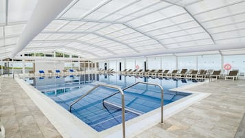A large indoor swimming pool with multiple lanes, lounge chairs, and a covered roof structure.