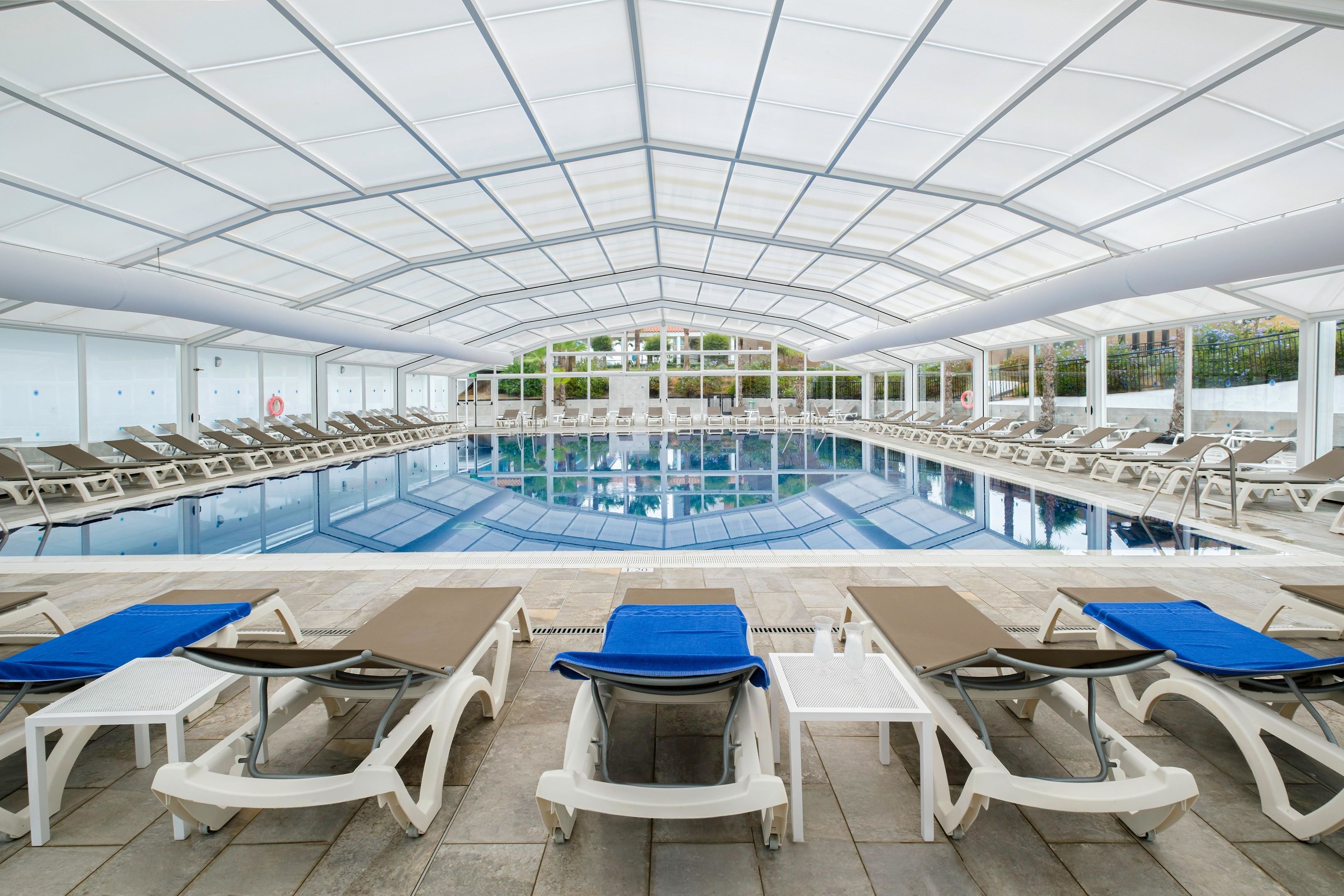 An indoor swimming pool with multiple lounge chairs and sunbeds arranged around it.