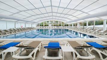 An indoor swimming pool with multiple lounge chairs and sunbeds arranged around it.