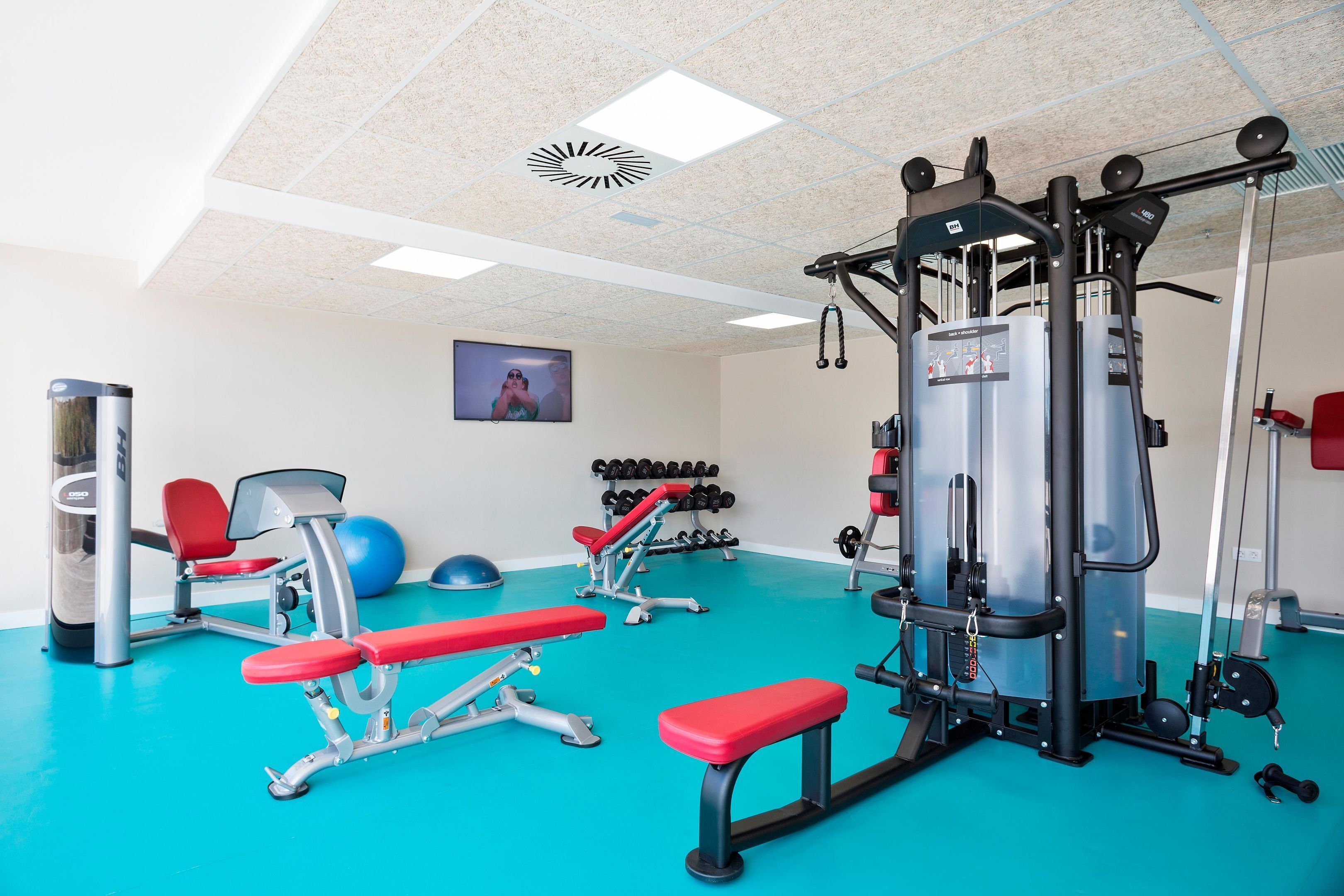 Ein Fitnessstudio mit Trainingsgeräten, Bänken und einem an der Wand befestigten Fernseher.