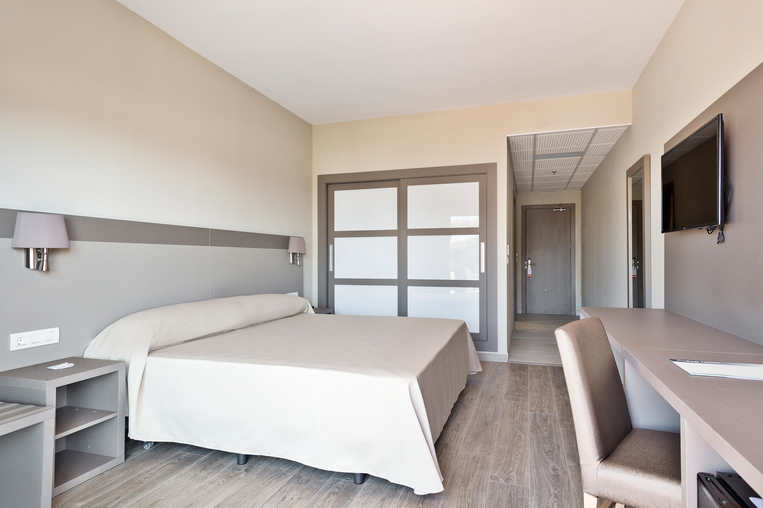 Ein Hotelzimmer mit Bett, Schreibtisch, Stuhl, Fernseher und einem durch eine Glastür einsehbaren Badezimmer.