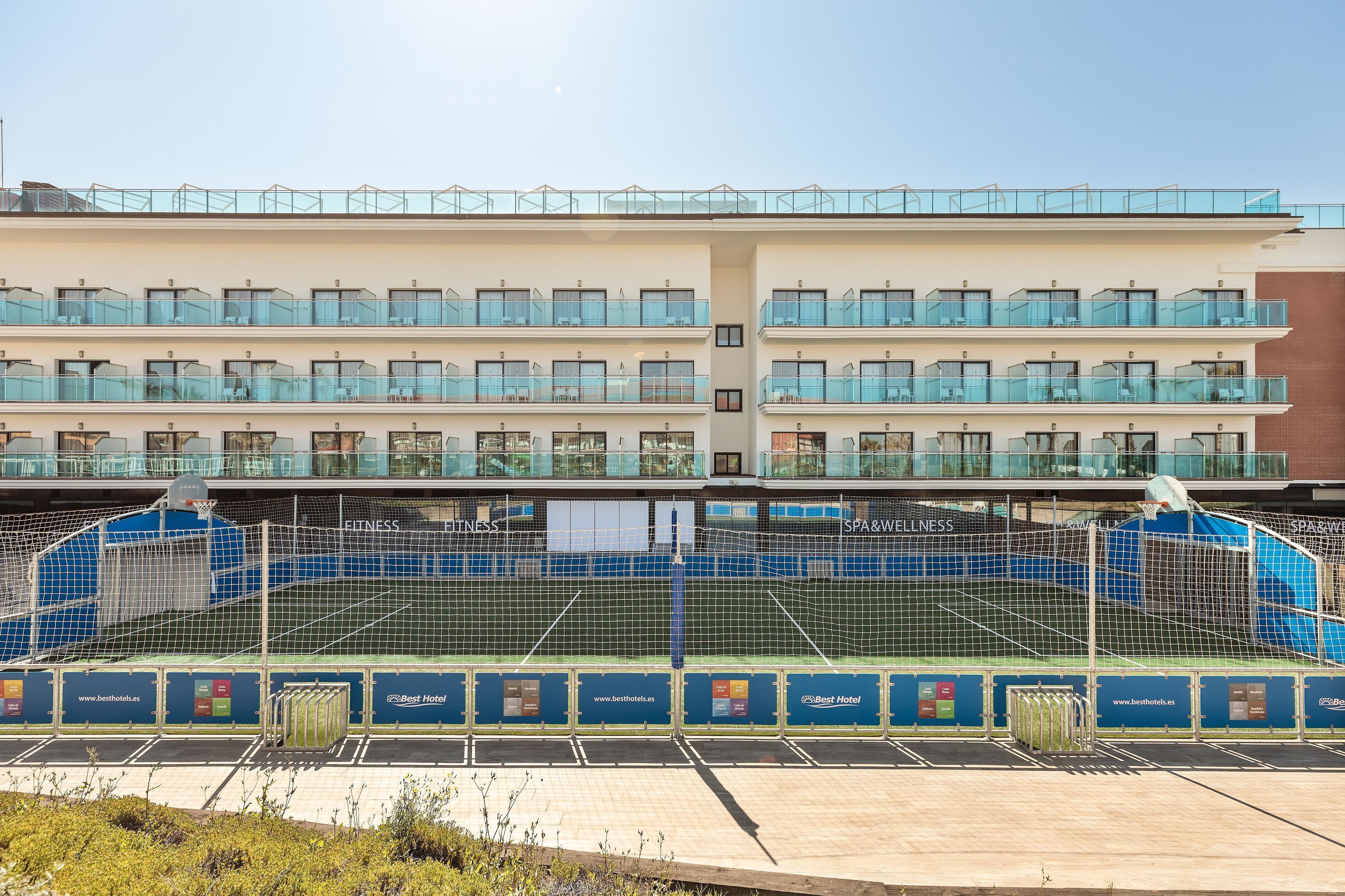 A hotel with multiple balconies, a swimming pool, and a clear sky.