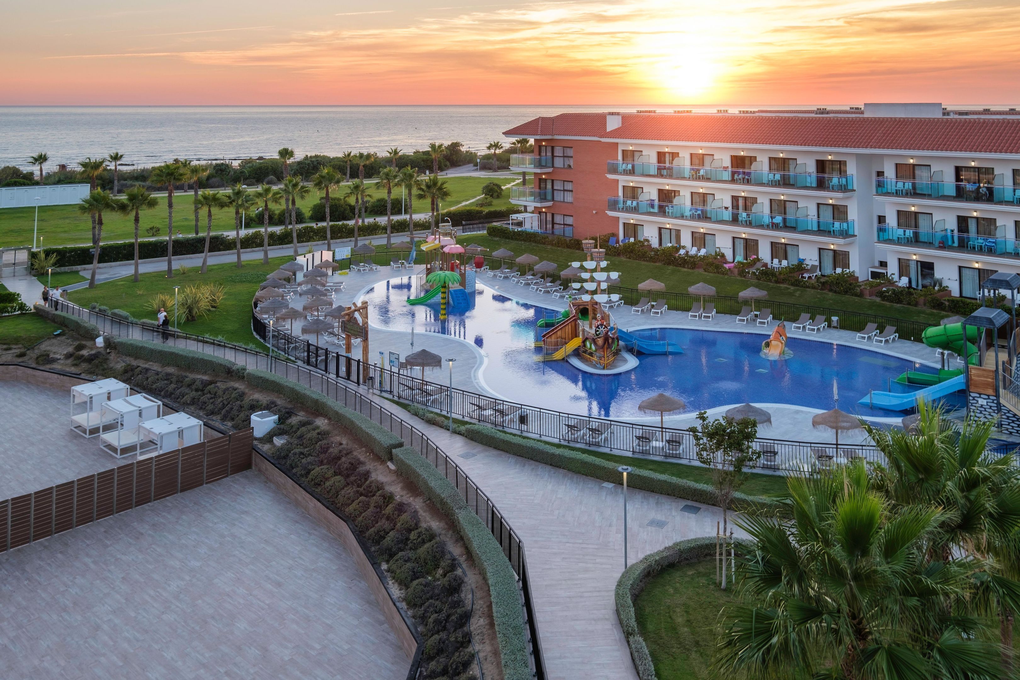A resort with a swimming pool, water slides, and a view of the sunset over the ocean.