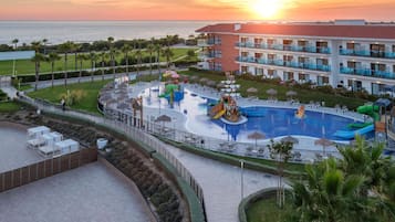 A resort with a swimming pool, water slides, and a view of the sunset over the ocean.