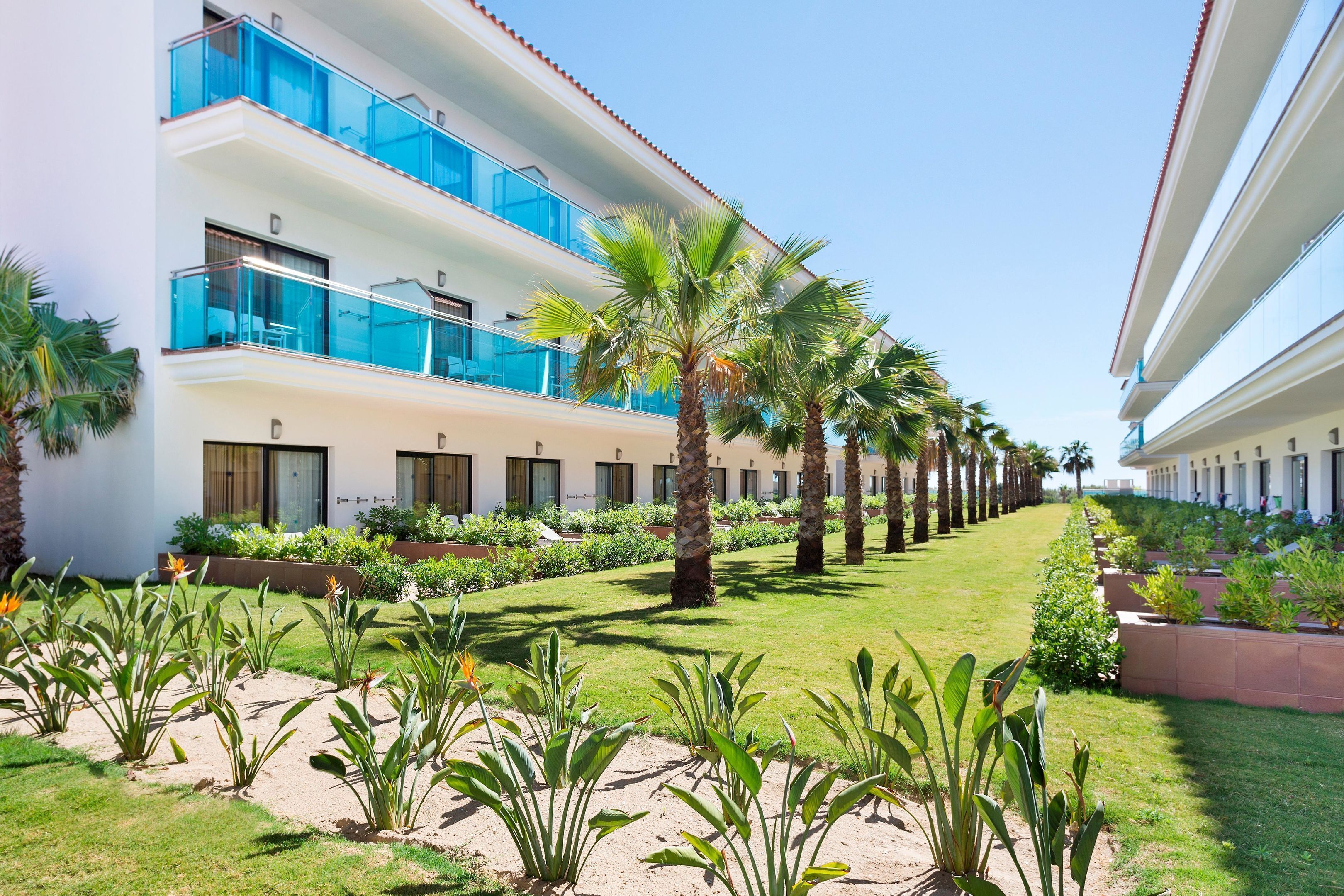 A hotel with multiple floors, outdoor palm trees, and a well-maintained garden area.