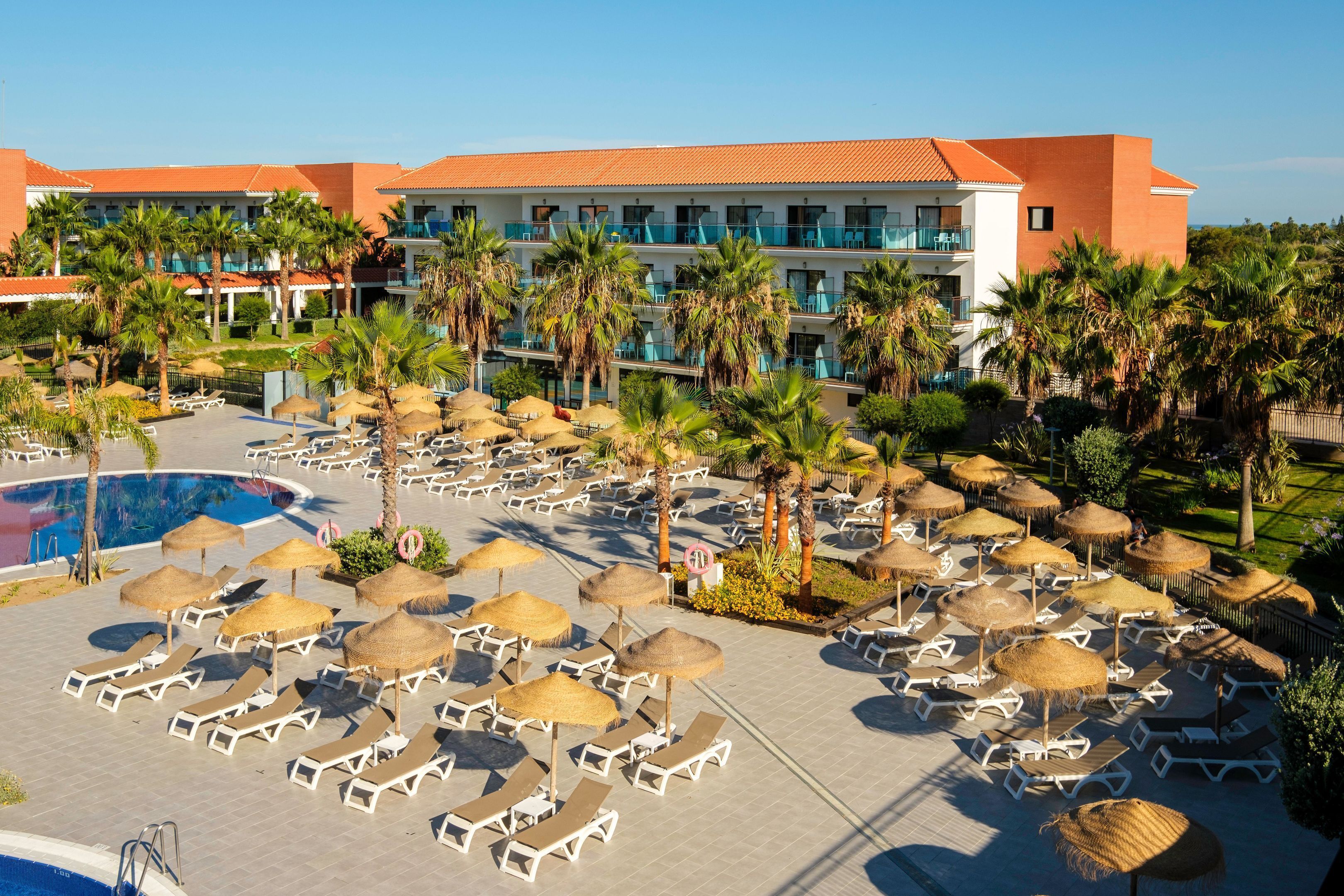 A resort with a pool area, sun loungers, and palm trees.