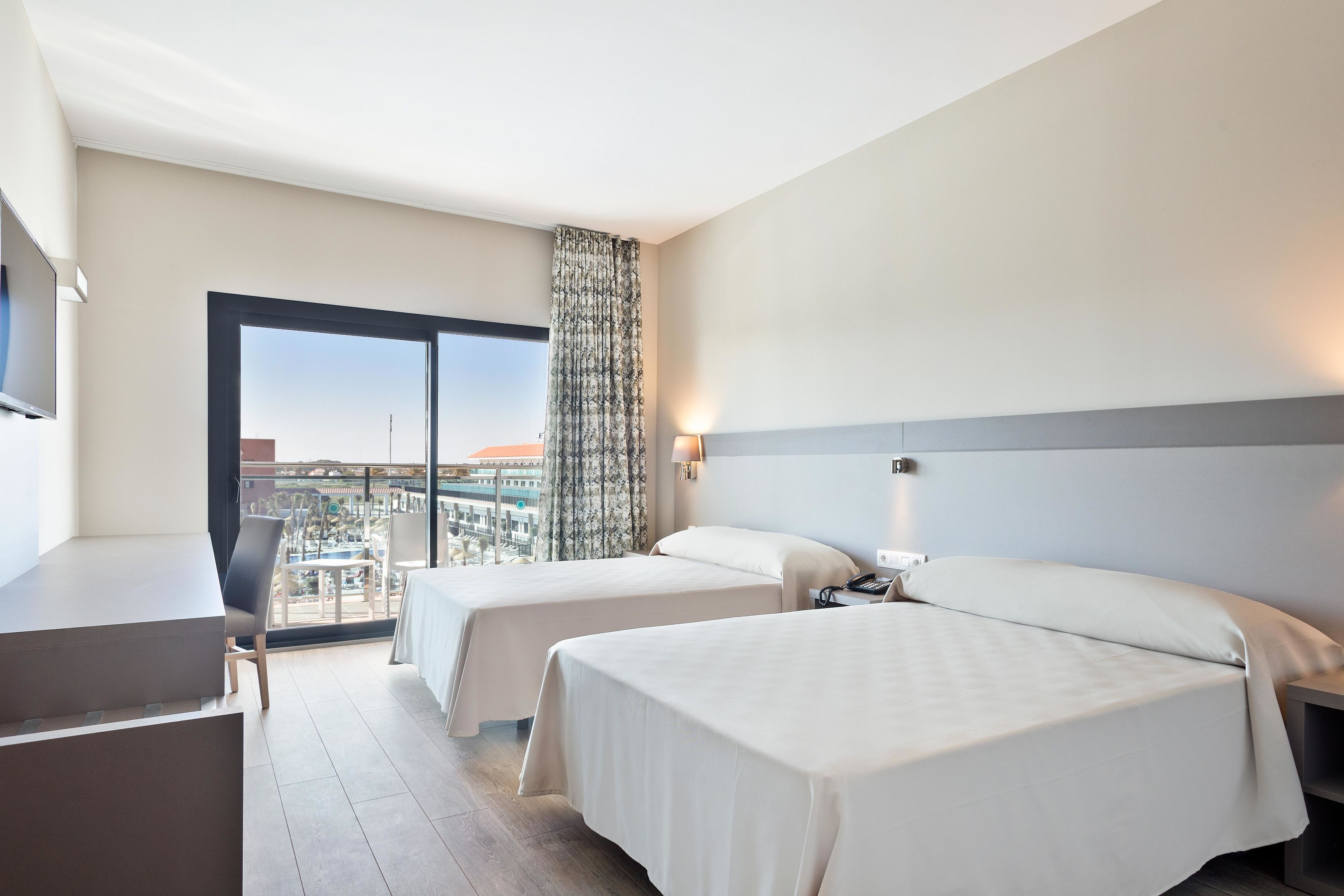 Ein Hotelzimmer mit zwei Betten, einem Schreibtisch und einem großen Fenster mit Blick auf die Stadt.
