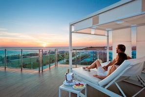 Una pareja relajándose en una tumbona con vistas a la puesta de sol sobre el océano.