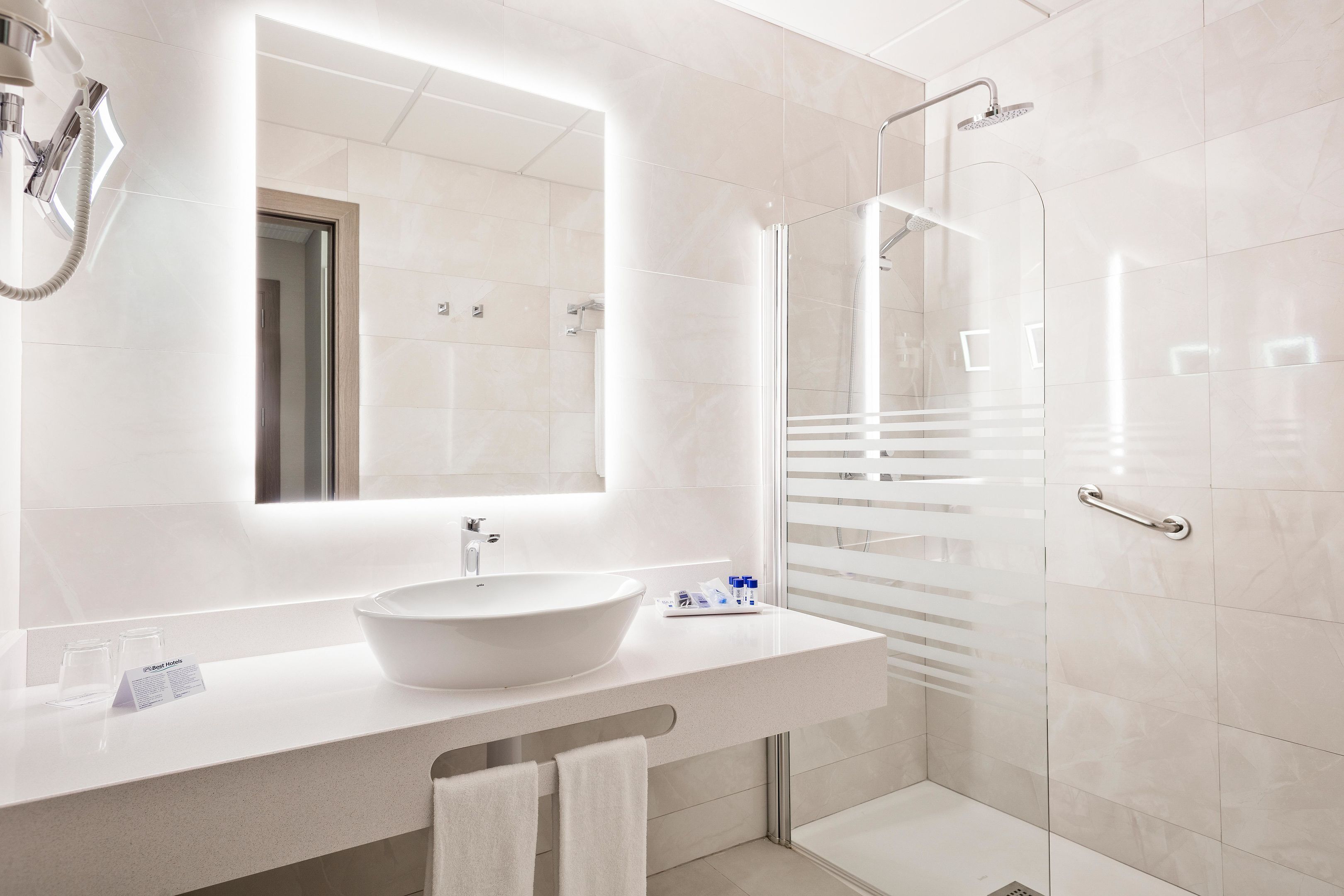 A modern bathroom with a large white sink, a mirror, and a glass-enclosed shower.