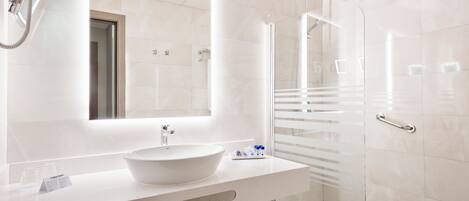 A modern bathroom with a large white sink, a mirror, and a glass-enclosed shower.