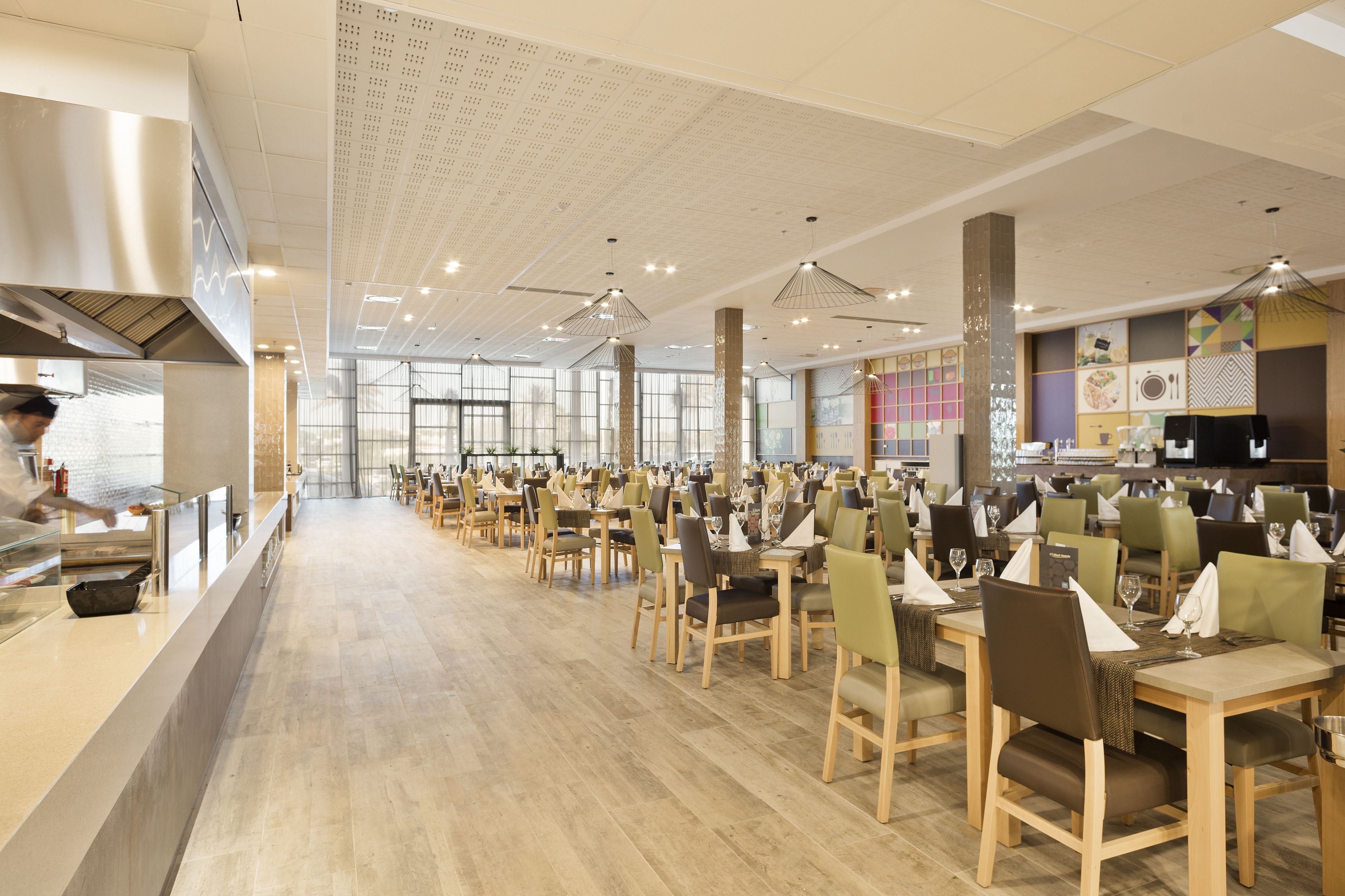 A spacious restaurant with multiple dining tables and chairs, a long counter, and a modern ceiling design.