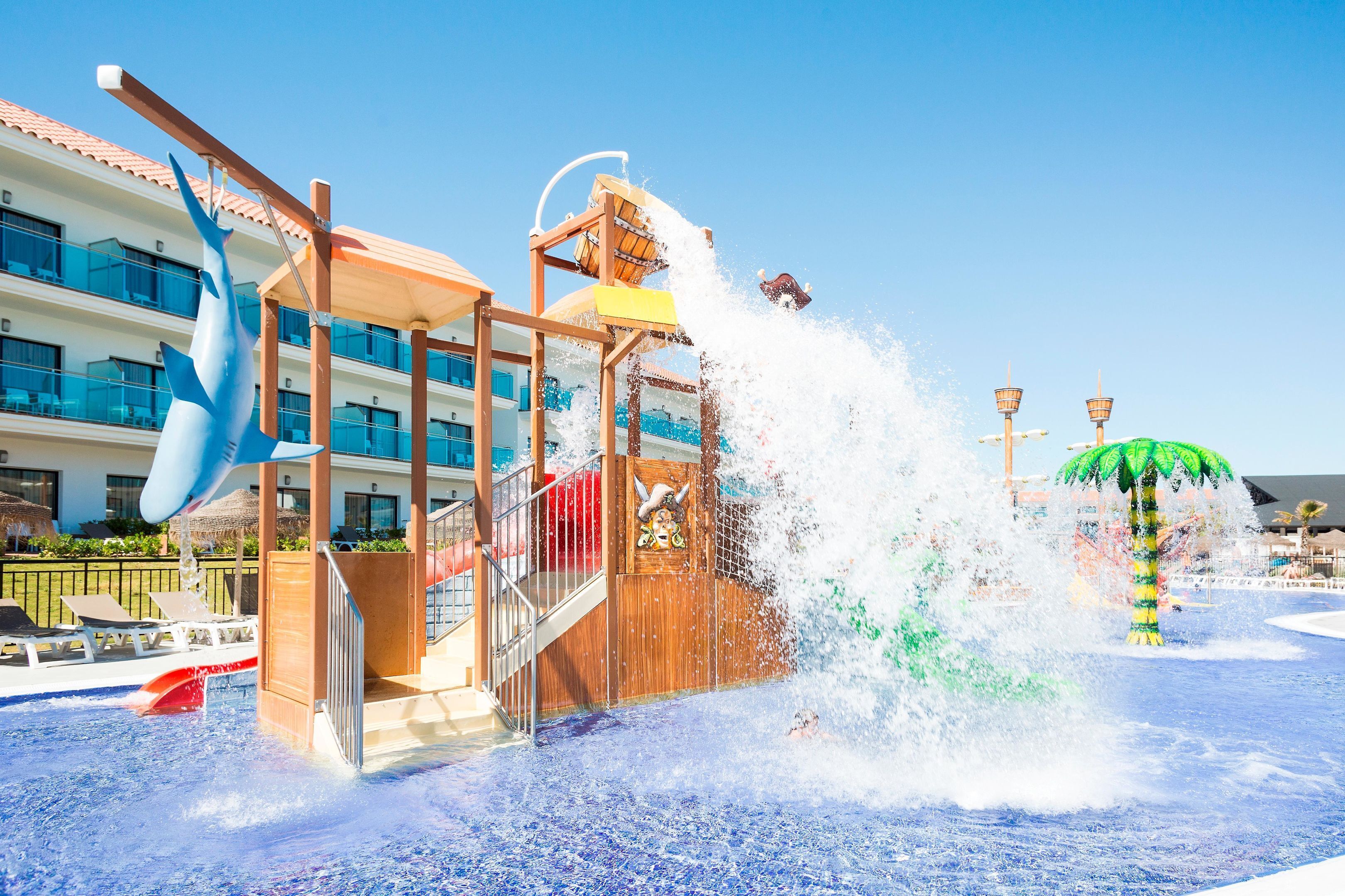 A water play area with a shark, a slide, and a palm tree.