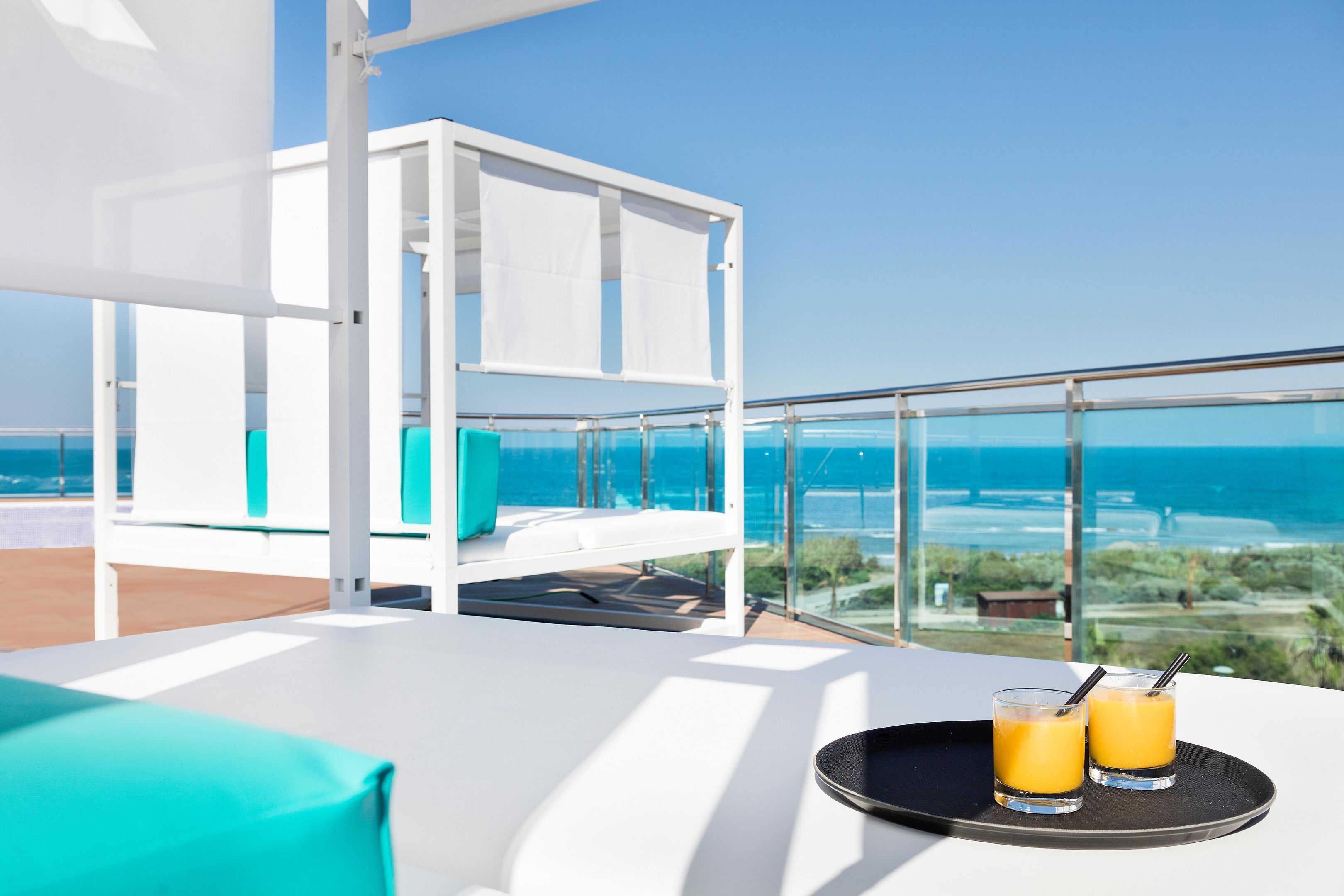 Een balkon met een witte bank en een glazen tafel met twee glazen sinaasappelsap.