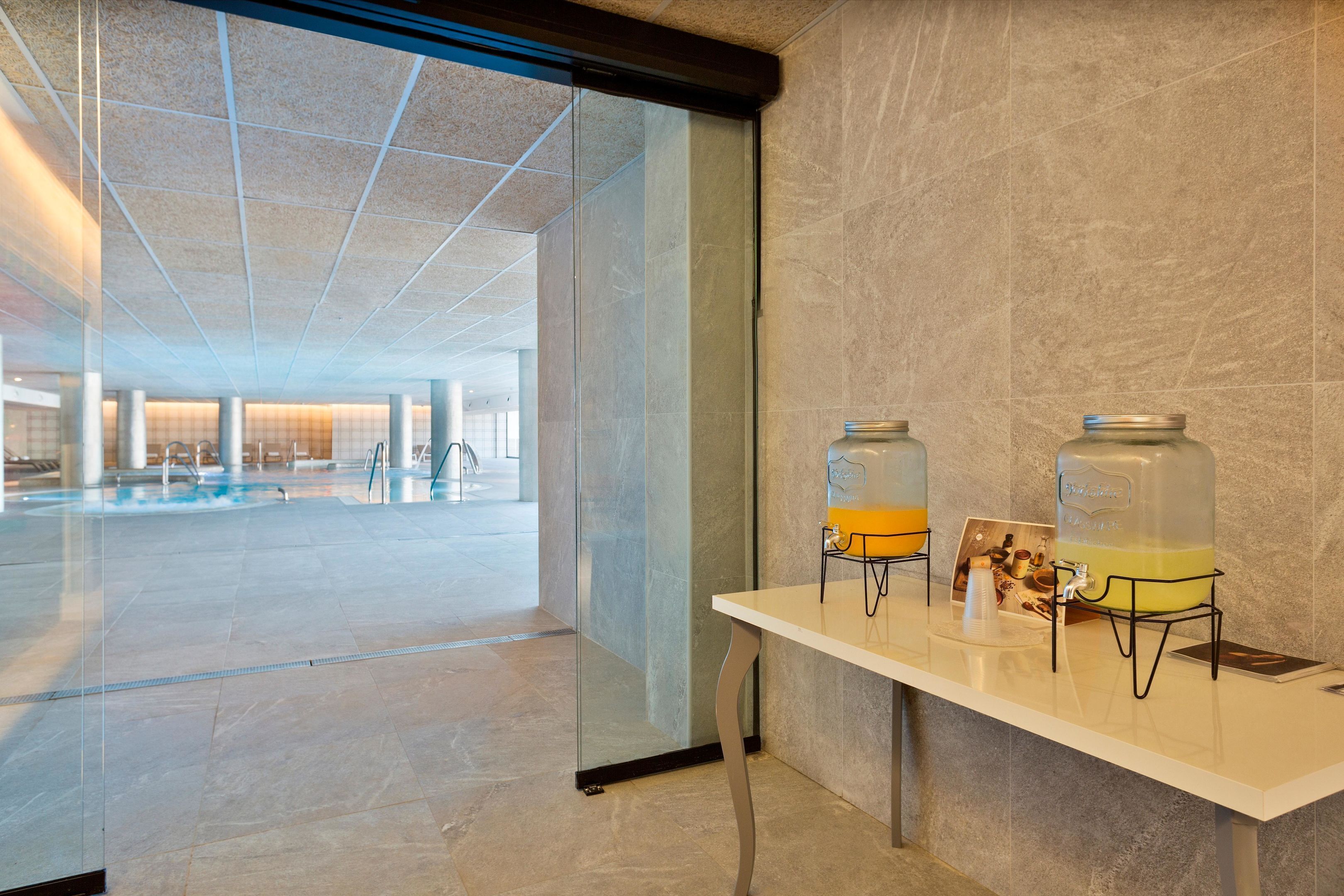 A modern hotel lobby with a glass wall, a reception desk, and two large water dispensers.