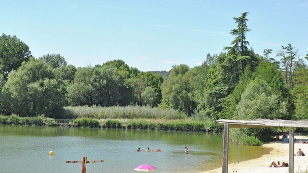 Un cadre idyllique au bord d’un lac, où l’on peut voir des gens se baigner et se détendre sur la plage.