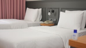 Hotellihuone, jossa on kaksi sänkyä, sängyn vieressä puhelin ja yöpöytä.