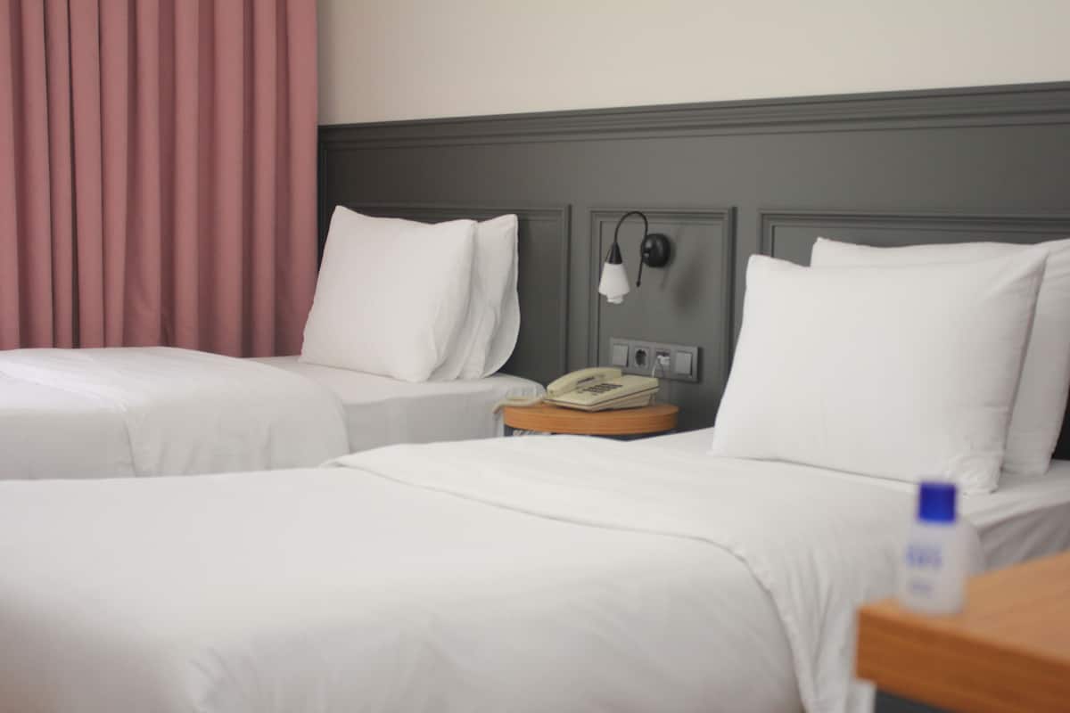 Une chambre d’hôtel avec deux lits, un téléphone sur la table de chevet et une petite table de nuit.