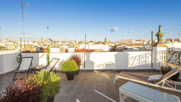 Una terrazza sul tetto con poltrone relax, piante in vaso e vista sulla città.