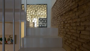 Una scala con gradini bianchi che conduce a un pianerottolo, una porta in vetro decorata con motivi circolari e un muro in mattoni.