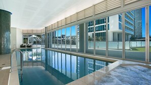 Una piscina interior con paredes de vidrio transparente, vistas al exterior y una zona de hidromasaje.