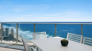Un balcón con mesa y sillas blancas, con vista a una playa y al océano.