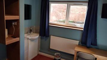 Una habitación pequeña y funcional con ventana, radiador, lavabo, silla y estante con espejo.