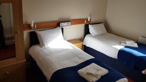Quarto de hotel com duas camas de solteiro, cabeceira de madeira, mesinhas de cabeceira pequenas em madeira e um radiador.