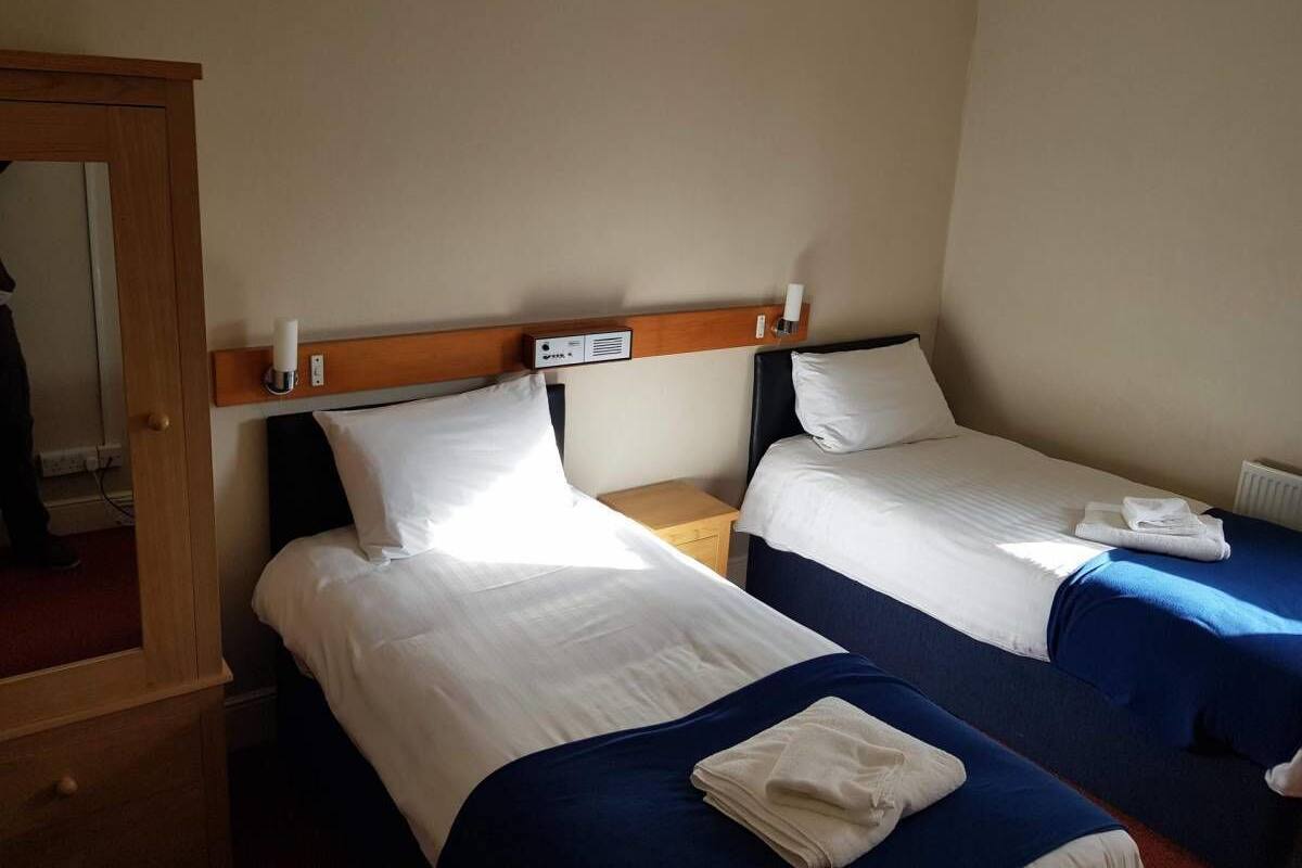 A hotel room with two single beds, a wooden headboard, a small wooden nightstand, and a radiator.