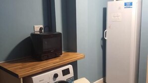 Uma área de lavanderia compacta com máquina de lavar, secadora e um eletrodoméstico alto, possivelmente um aquecedor, em frente a uma parede azul.