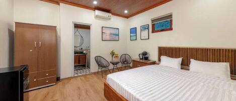 A bedroom with a wooden ceiling, a bed with white bedding, a wardrobe, a desk, two chairs, and a small table with a plant.