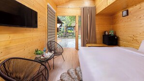 Ein Zimmer in einer Holzhütte, ausgestattet mit einem Bett, einem Fernseher, einem kleinen Tisch mit Stühlen und Blick auf den Garten.
