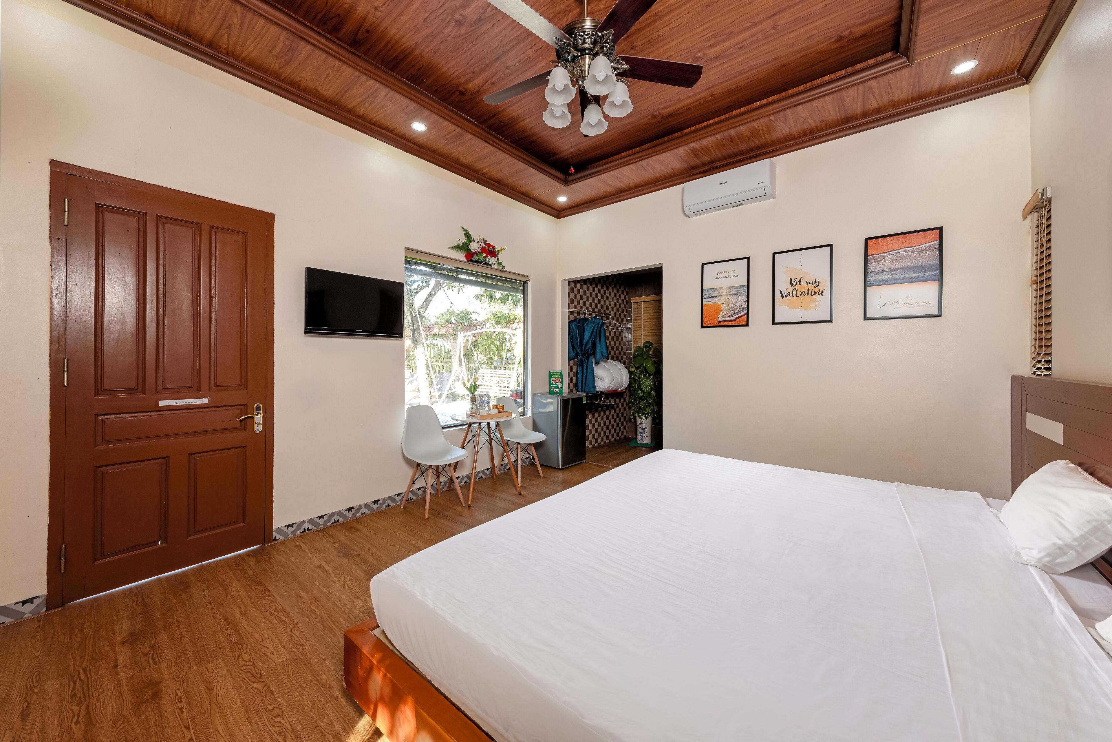 Une chambre avec un plafond en bois, un lit, un bureau avec des chaises et un téléviseur fixé au mur.