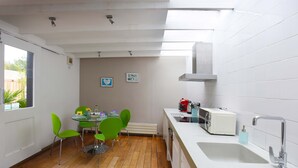 A modern kitchen with a dining area, featuring a wooden floor, white tiles, and green chairs. - Cedar House at The Old Fire Station (Canterbury)